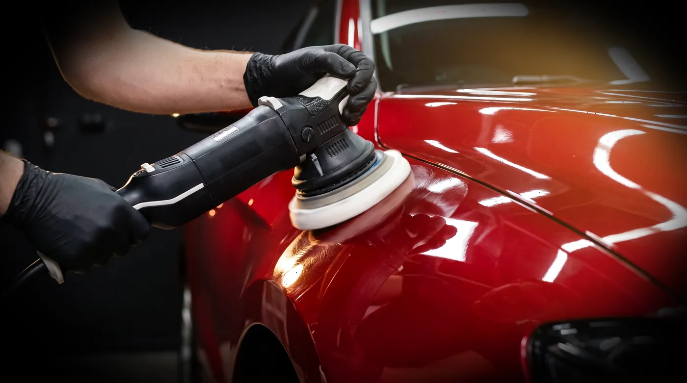 A dual-action polisher cutting swirls back from a glossy red car panel